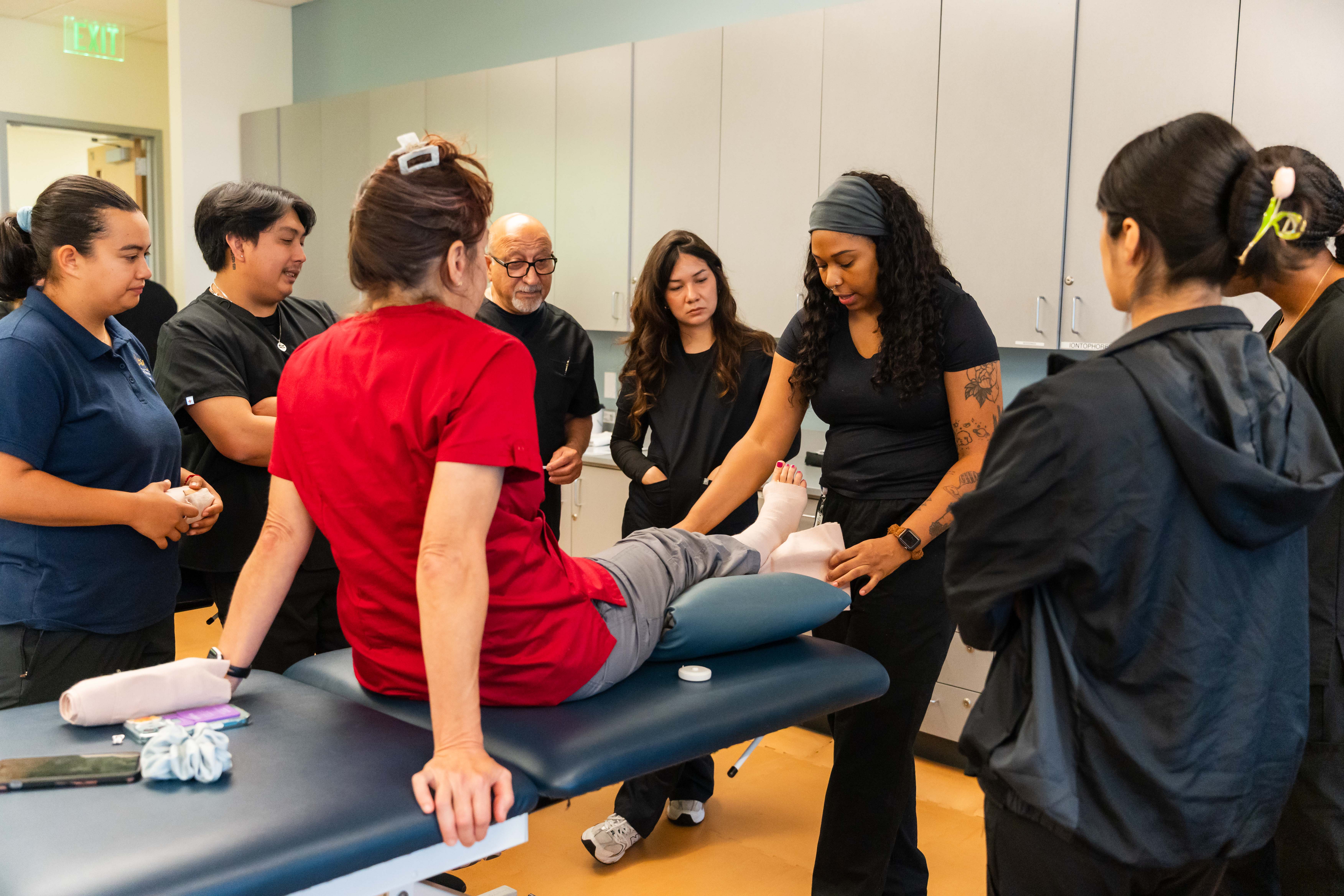 San Diego Mesa College Physical therapy students practice lower leg treatment techniques on a patient seated on an exam table in a classroom lab. 